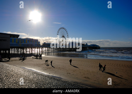 central pier and beach with people walking on sand late afternoon silhouetted against sun blackpool lancashire england uk europe Stock Photo