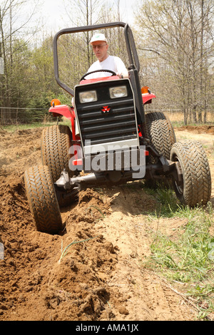 Man driving a small tractor ploughing or plowing field on specialist farm Stock Photo