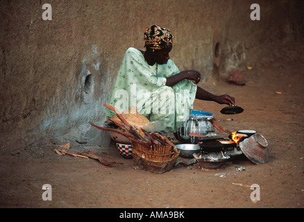 A young woman squatting in the street with her pans and charcoal stove as a pancake vendor in Mali Africa Stock Photo