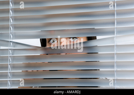 A young woman peering through Venetian blinds Stock Photo