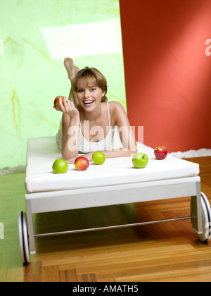 Woman lying on bed with apples, smiling Stock Photo