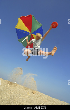 young man with frisbee and sunshade jumping on the beach Stock Photo