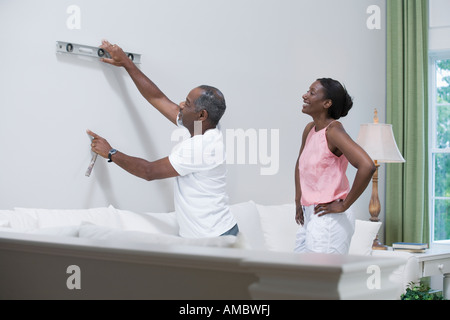 Middle-aged man using spirit level on a wall with a middle-aged woman standing behind him and smiling Stock Photo