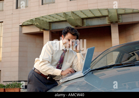 VEP72165 Young Indian Executive with tie smiling and talking on mobile phone and working on computer Stock Photo
