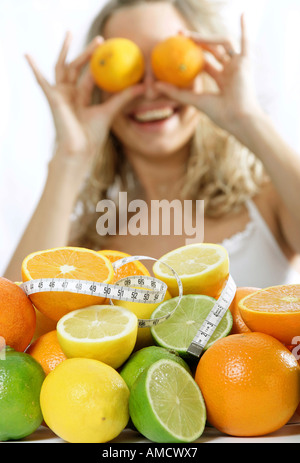 Woman holding orange and lime on eyes focus on fruits wrapped with measuring tape Stock Photo