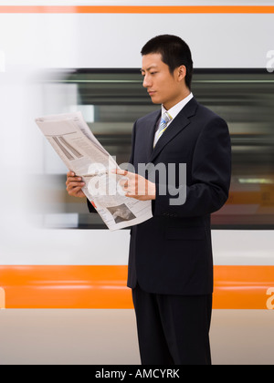 Businessman reading newspaper with subway in background Stock Photo