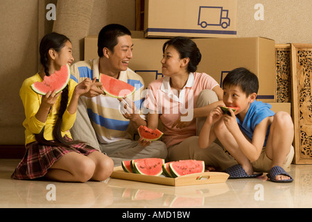 Family of four eating watermelon and smiling with cardboard boxes in background Stock Photo