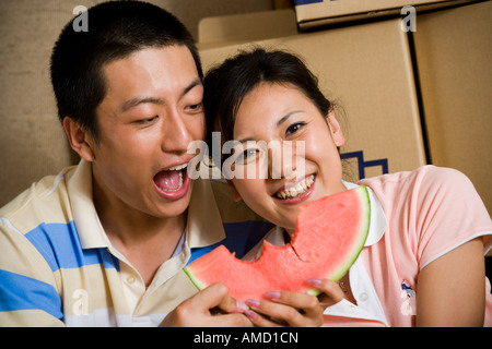 Couple sharing watermelon and smiling with cardboard boxes in background Stock Photo