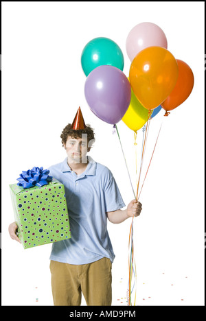 Man with party hat holding balloons and gift box looking sad Stock Photo