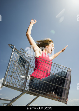 Woman in shopping cart outdoors with arms up smiling Stock Photo