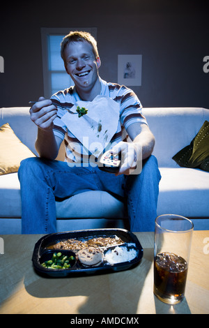 Man on sofa with frozen dinner and napkin with food smiling Stock Photo