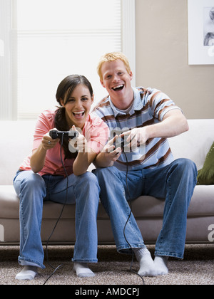 Man and woman sitting on sofa playing video games laughing Stock Photo