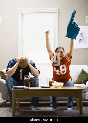 Man and woman sitting on sofa watching football smiling and cheering Stock Photo