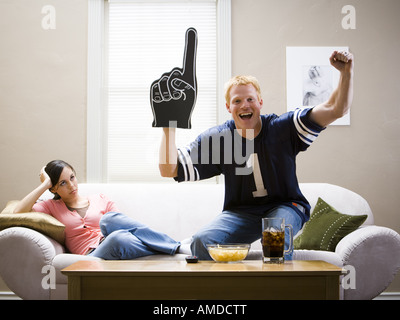 Woman on sofa and man in football jersey standing and cheering Stock Photo
