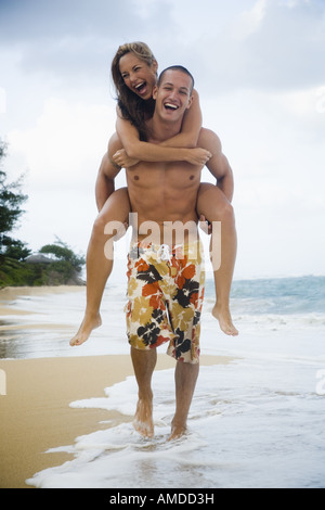 Man giving woman piggyback ride on beach Stock Photo