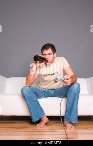 Man playing games console whilst drinking from a brown bottle Stock Photo