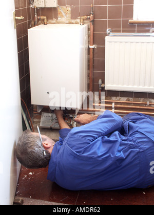 Back view plumber & heating engineer working in house interior on gas central heating boiler checking copper pipework & controls in house England Uk Stock Photo