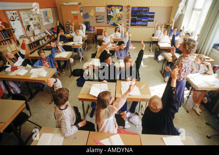 Elementary school children sitting at individual desks in Swedish classroom raising hands to answer questions from the teacher Stock Photo