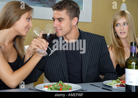 young couple drinking red vine, blond woman watching envious Stock Photo