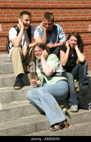 four teenagers talking on their mobile phones sitting on stairs in town Stock Photo