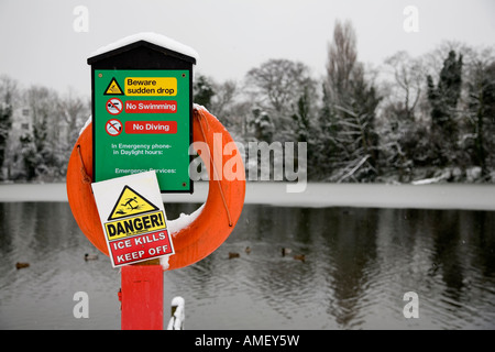 Bright orange lifebelt and green sign warning of danger, ice,no swimming, diving and sudden drop with water in background Stock Photo