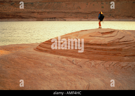 Woman Wearing Backpack Standing On Rock near Water Stock Photo