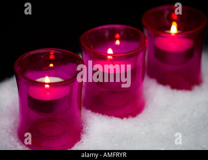 Candles in pink glass tealight holders shot standing in faux snow with alit  black background Stock Photo