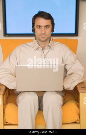 Man using a laptop with plasma screen in background Stock Photo