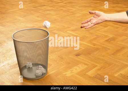 mans hand throwing scrunched up ball of paper into bin Stock Photo