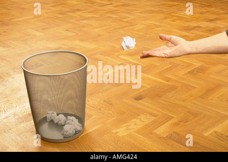 mans hand throwing scrunched up crunched ball of paper into a waste paper bin basket Stock Photo