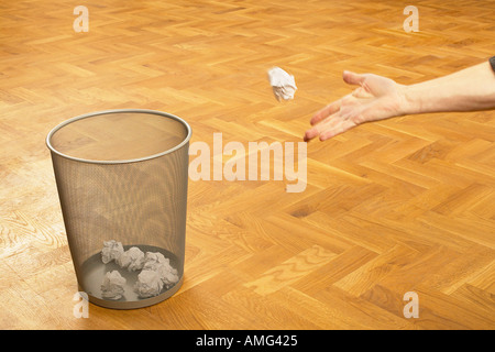 mans hand throwing scrunched up crunched ball of paper into a waste paper bin basket Stock Photo