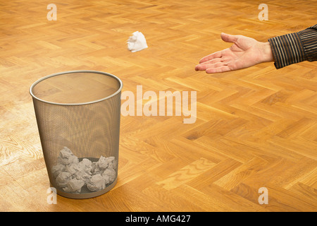 mans hand throwing scrunched up crunched ball of paper into a waste paper bin basket Stock Photo