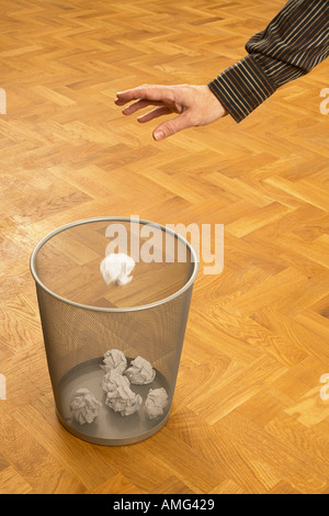 mans hand throwing scrunched up crunched ball of paper into a waste paper bin basket Stock Photo