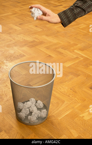 mans hand throwing scrunched up crunched ball of paper into a waste paper bin basket Stock Photo