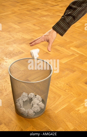 mans hand throwing scrunched up crunched ball of paper into a waste paper bin basket Stock Photo