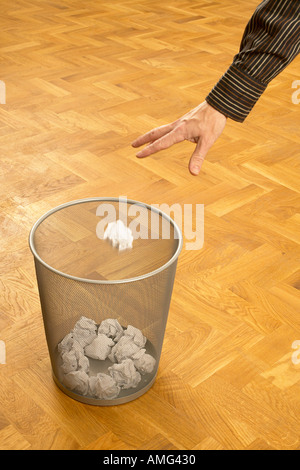 mans hand throwing scrunched up crunched ball of paper into a waste paper bin basket Stock Photo