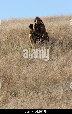 A Native American Indian man crouching in the dead grasses hunting game ...