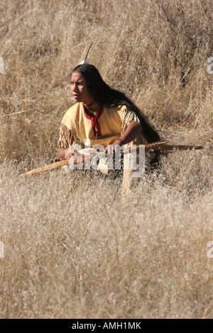 A Native American Indian boy crouching in the dead grasses hunting game with a bow and arrow Stock Photo