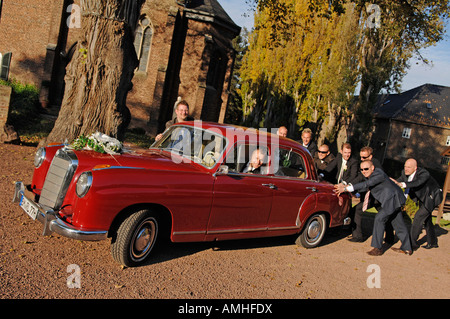 Groom sitting in old Mercedes wich is pushed by his friends Stock Photo