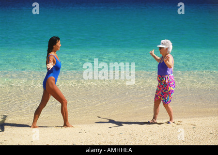 80 year old grandmother and 40 year old mother doing yoga and Tai Chi exercises on beach Stock Photo