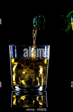 Whiskey being poured into a glass of ice against a black background Stock Photo