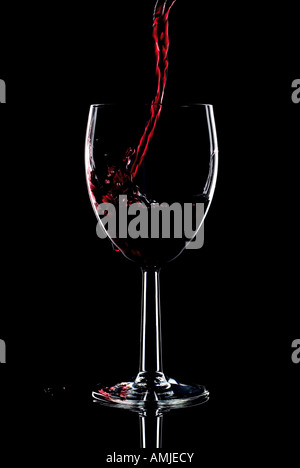 Red wine being poured into a glass and splashing over the side Low key black background Stock Photo