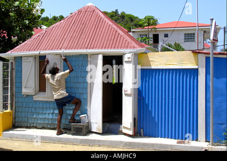 Man paints eaves of traditional blue wooden shingle building with red tin roof Gustavia St Barts Stock Photo