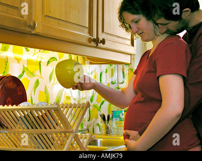 MR PR man kissing his pregnant woman while she is washing the dishes in the kitchen Stock Photo