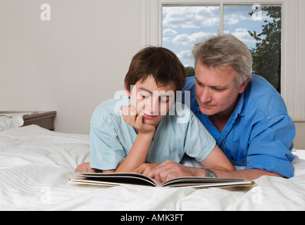Father and son reading book together on bed Stock Photo