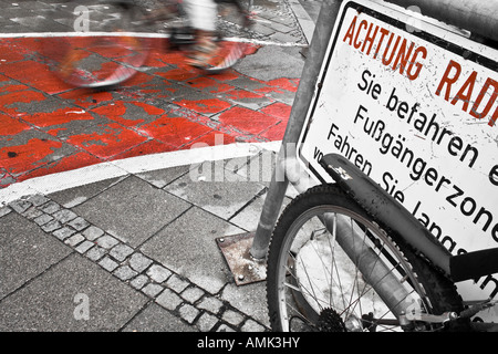 A cyclist on a cycle path in Munich. The sign to the left warns cyclists not to go fast as it is a padestrian zone. Stock Photo