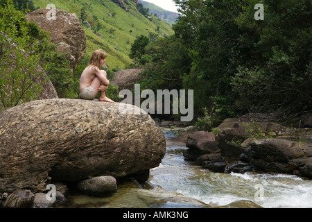 teenage girl sitting on rock looking at mountain stream in country side Stock Photo