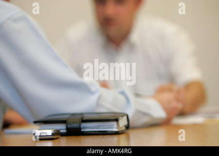 TWO MALE OFFICE WORKERS HAVING A MEETING,FOCUSED ON A MOBILE PHONE AND FILOFAX. Stock Photo