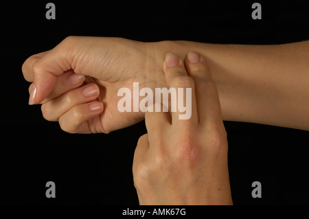 Female shown taking her own pulse isolated against a black background Stock Photo