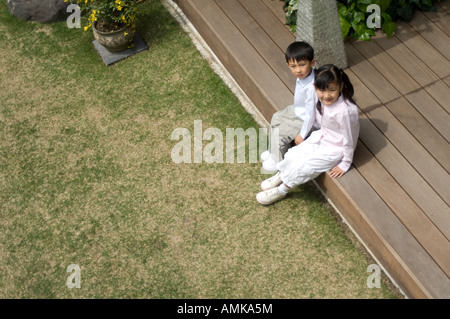 Boy and girl sitting on wooden deck Stock Photo